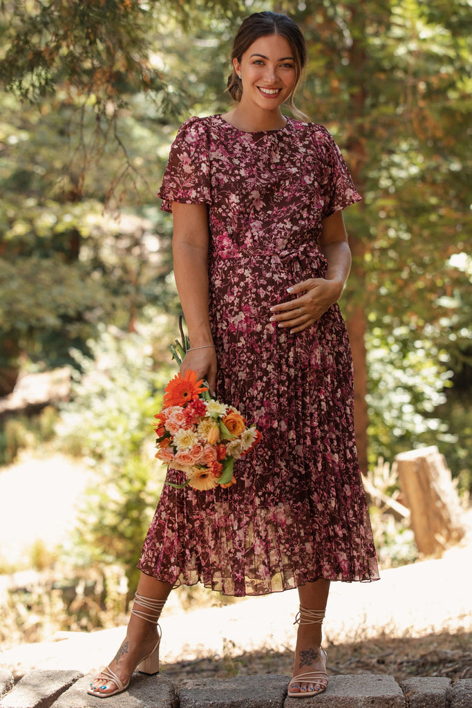 Woman in a floral dress standing outdoors with flowers in her hand