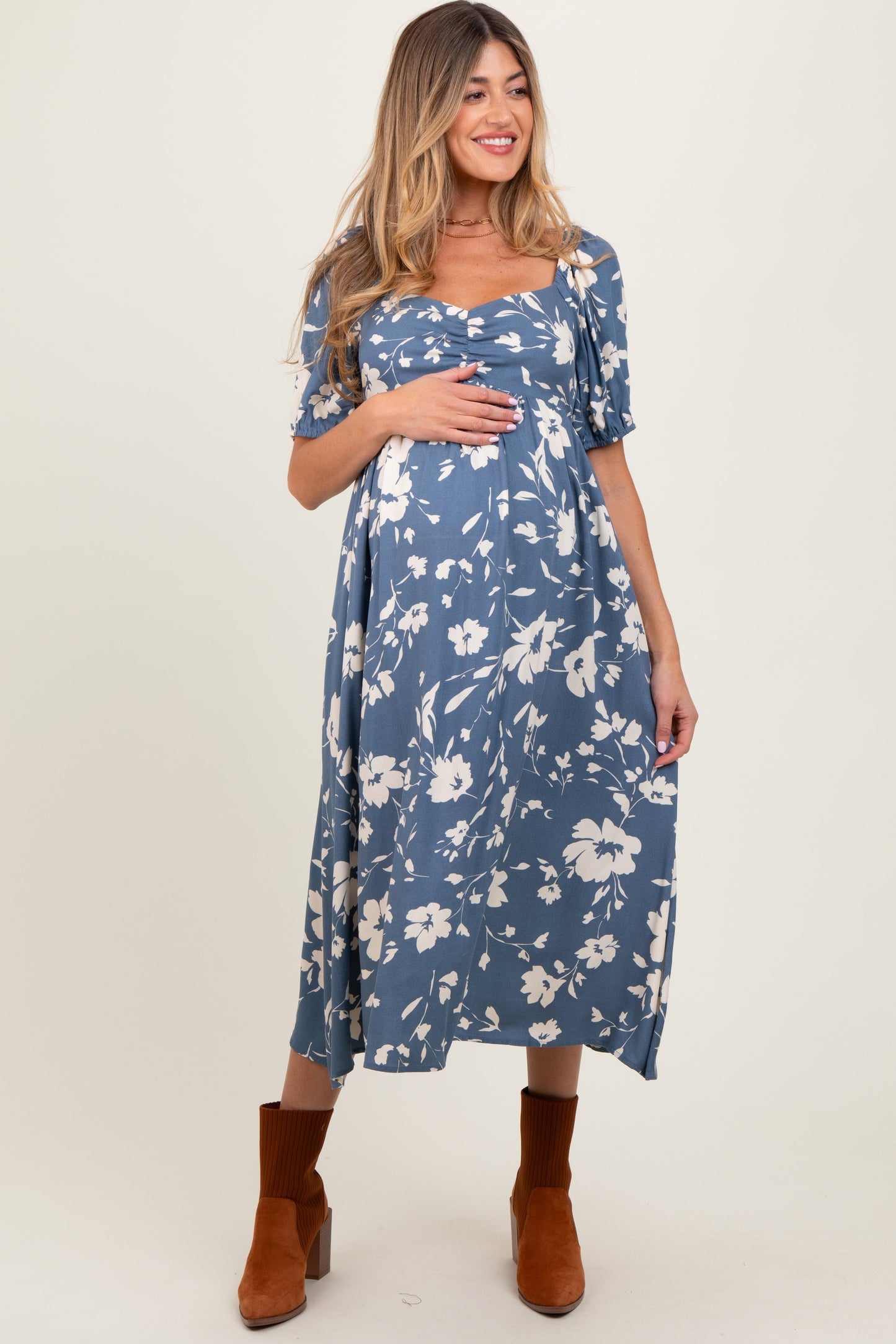 Woman wearing a blue floral dress with brown boots on a white background