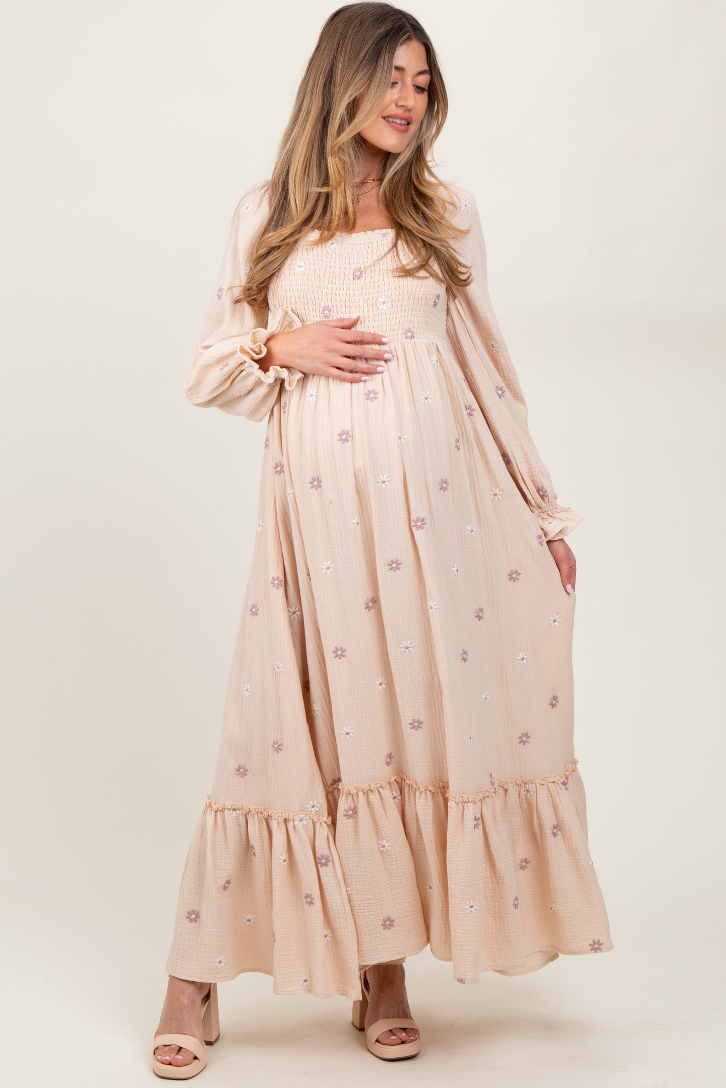 Woman wearing a long, light pink dress with floral patterns on a white background