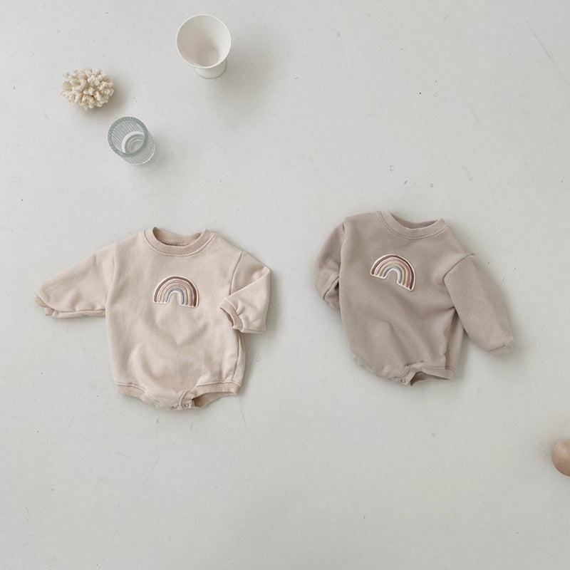 Two beige baby rompers with rainbow designs on a light gray surface.