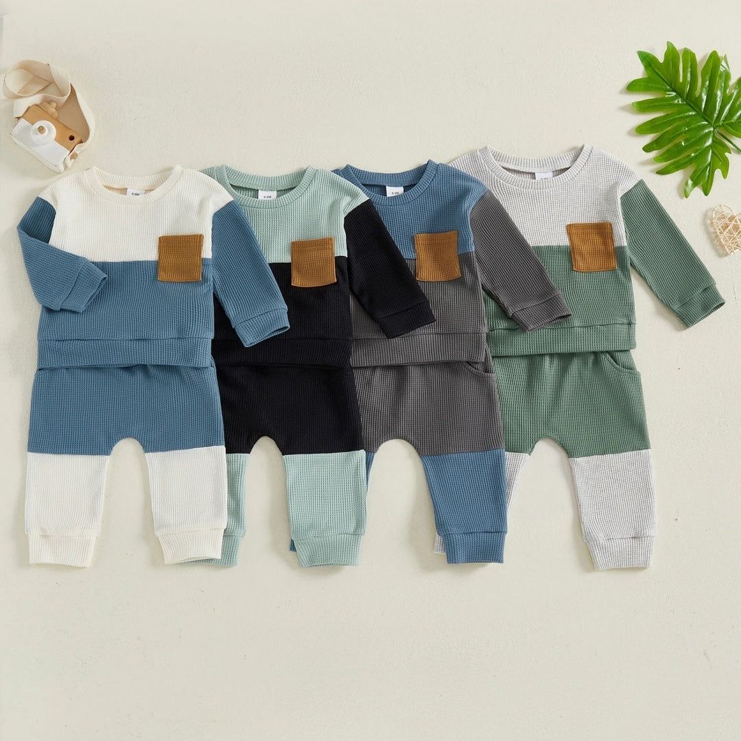 Four baby outfits in different color combinations on a light background with a toy and plant.