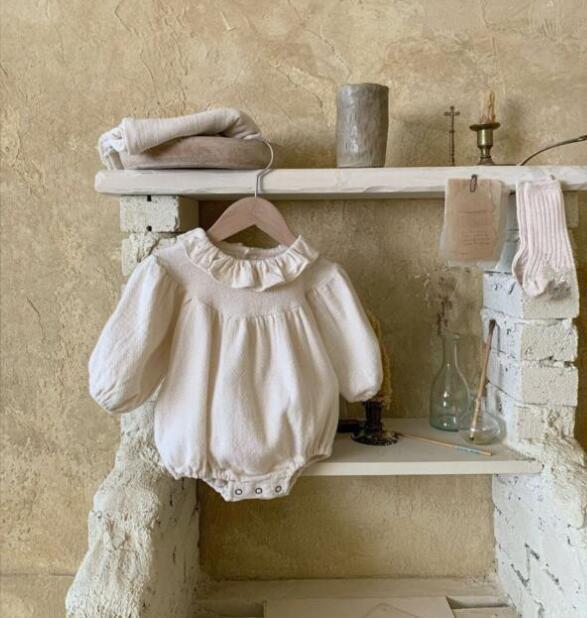 White baby romper on a hanger against a rustic stone wall.