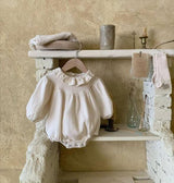 White baby romper on a hanger against a rustic stone wall.