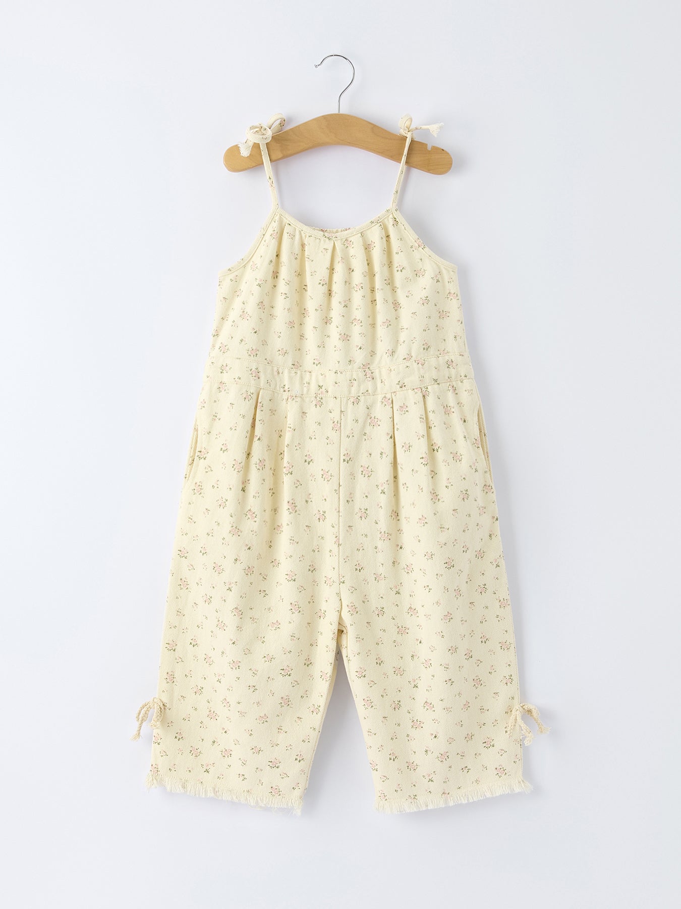 Yellow floral jumpsuit hanging on a wooden hanger against a white background