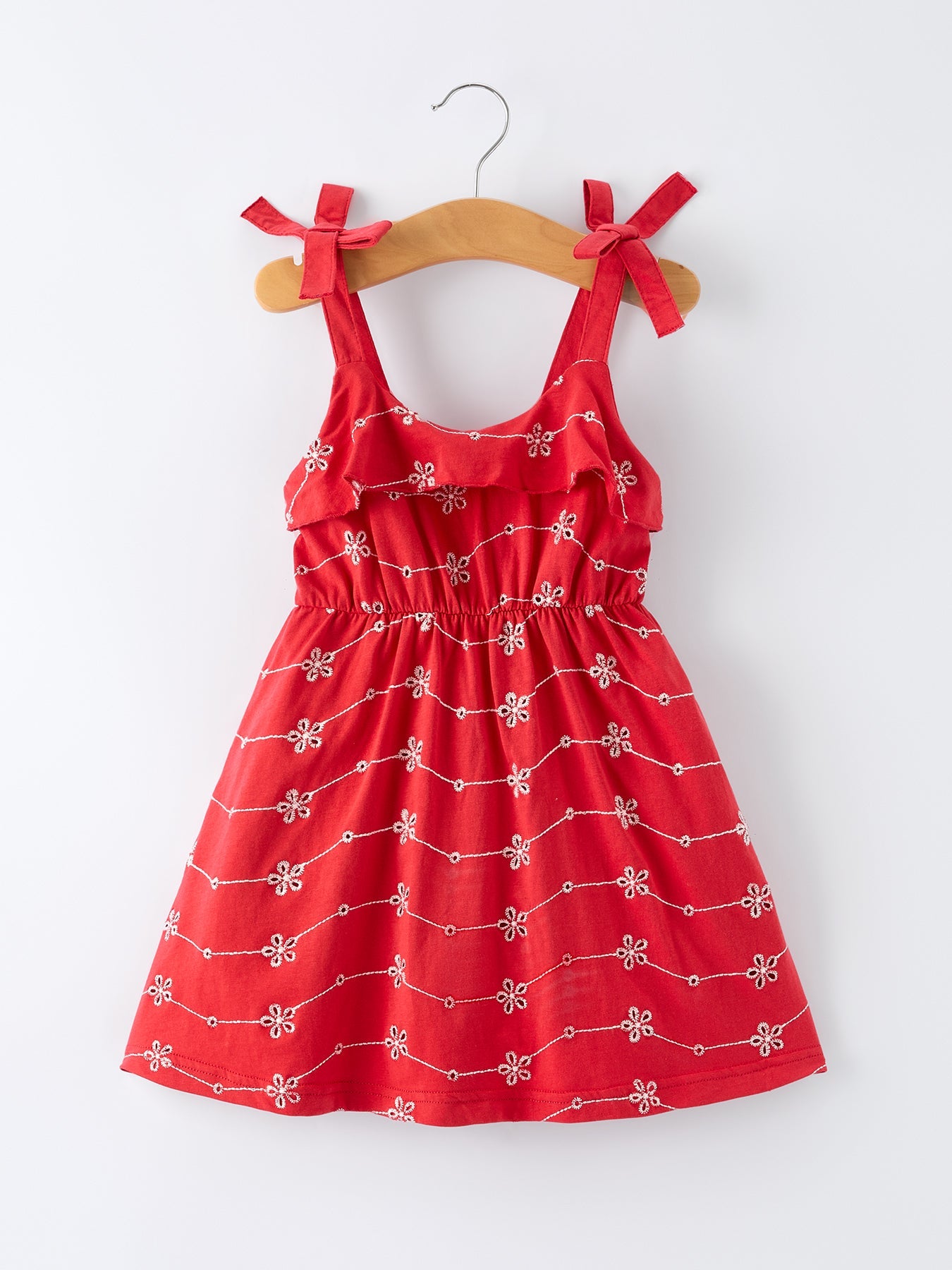 Red dress with white patterns on a wooden hanger against a white background