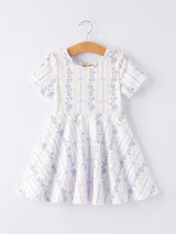 White dress with purple floral pattern on a hanger against a white background