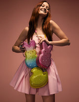 Woman holding colorful glittery Peeps-like bags against a brown background