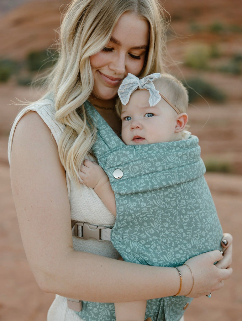 Woman holding a baby in a green baby carrier with a desert landscape in the background