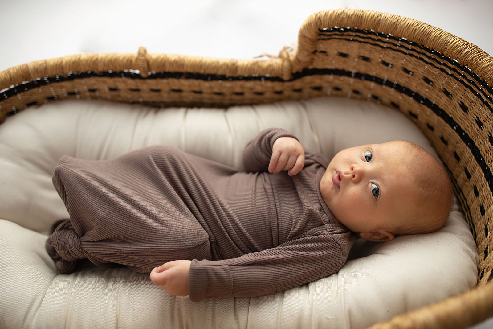 Ultra-soft, stretchy gender neutral baby gowns designed for comfort, featuring tie bottom and pull-down shoulder tabs for convenience. Cocoa Knotted Gown in a Snuggle Me Organics in a Plum + Sparrow Moses Baby Basket