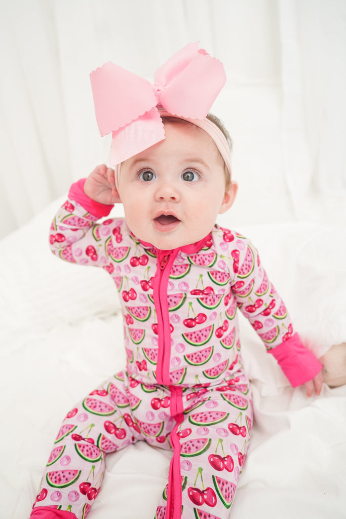 Baby in a pink and green patterned onesie with a large pink bow on a white background