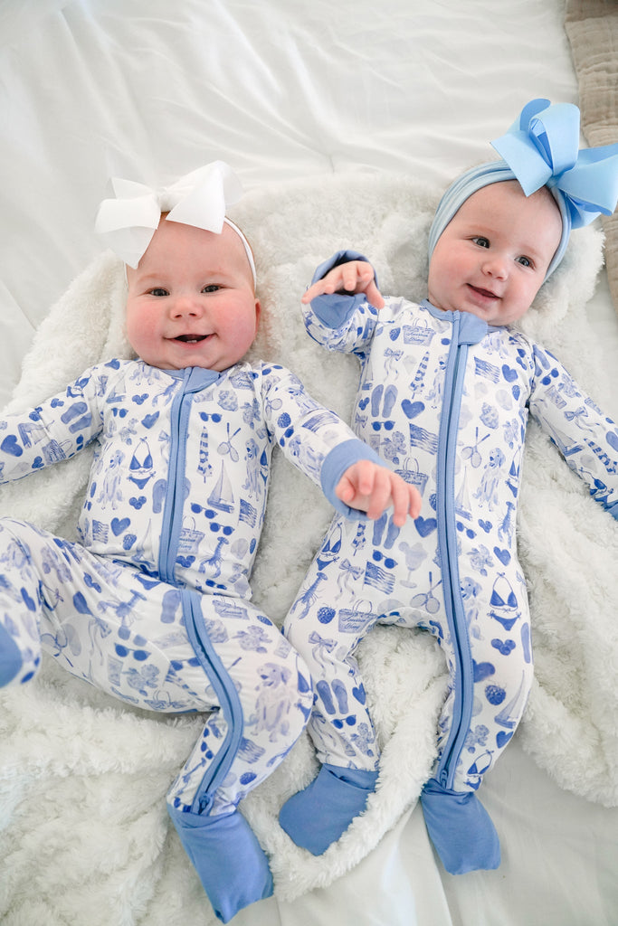 Two babies in matching blue and white outfits with bows on a soft surface