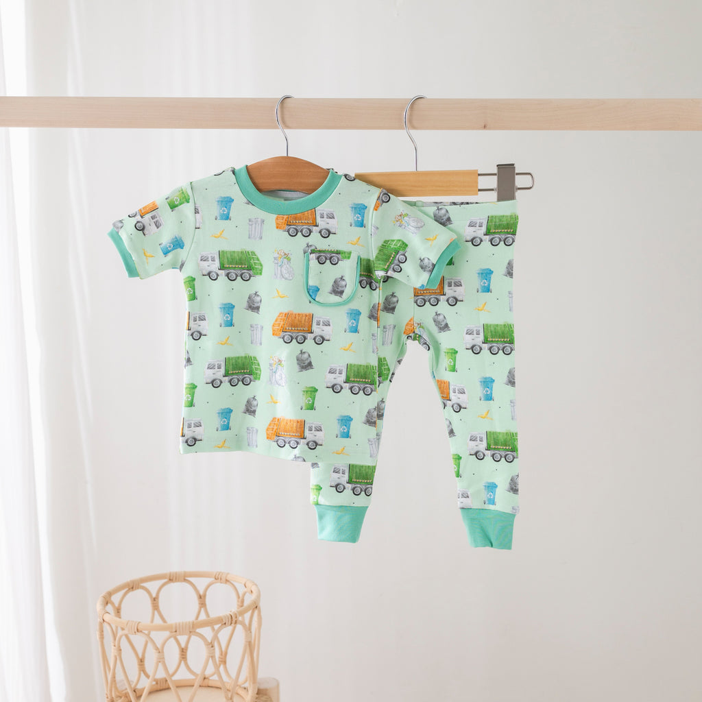 Children's pajama set with truck pattern on a wooden hanger against a white background.