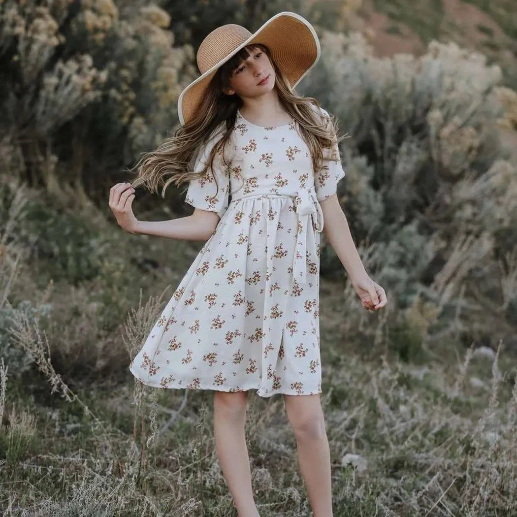 Woman in a floral dress and wide-brimmed hat standing in a natural setting