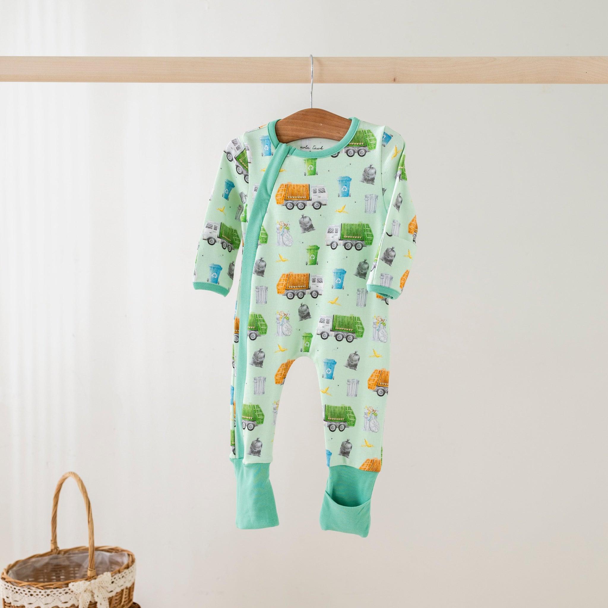 Children's onesie with vehicle pattern on a hanger against a white wall.