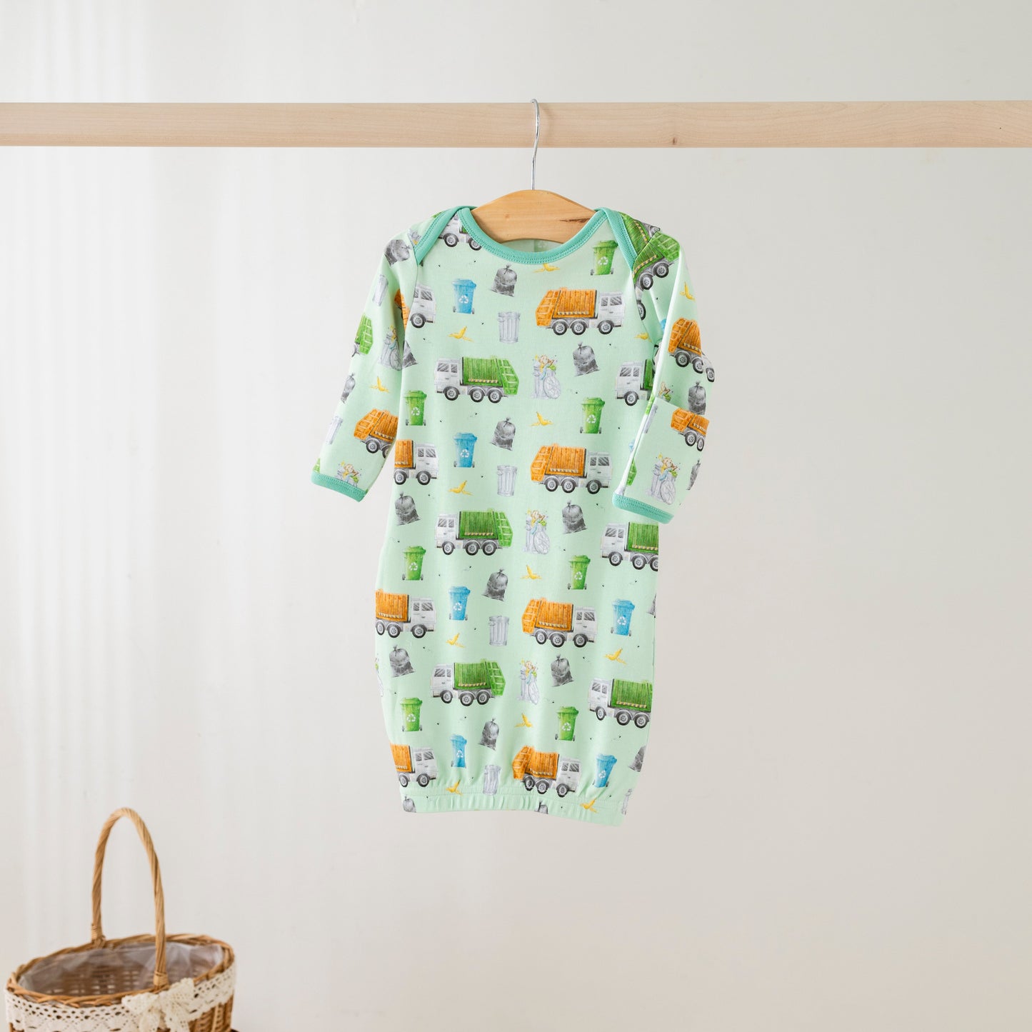 Baby onesie with vehicle pattern hanging on a wooden rod against a white wall.
