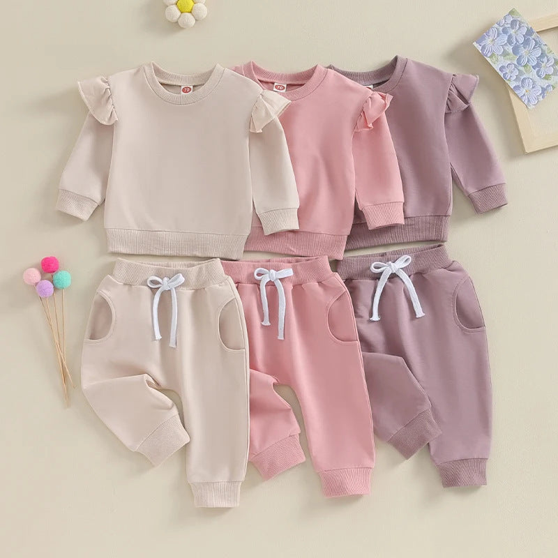 Three baby outfits in beige, pink, and purple with matching pants on a light background.