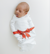 Newborn baby wrapped in a white blanket with a red bow and text on a light gray background