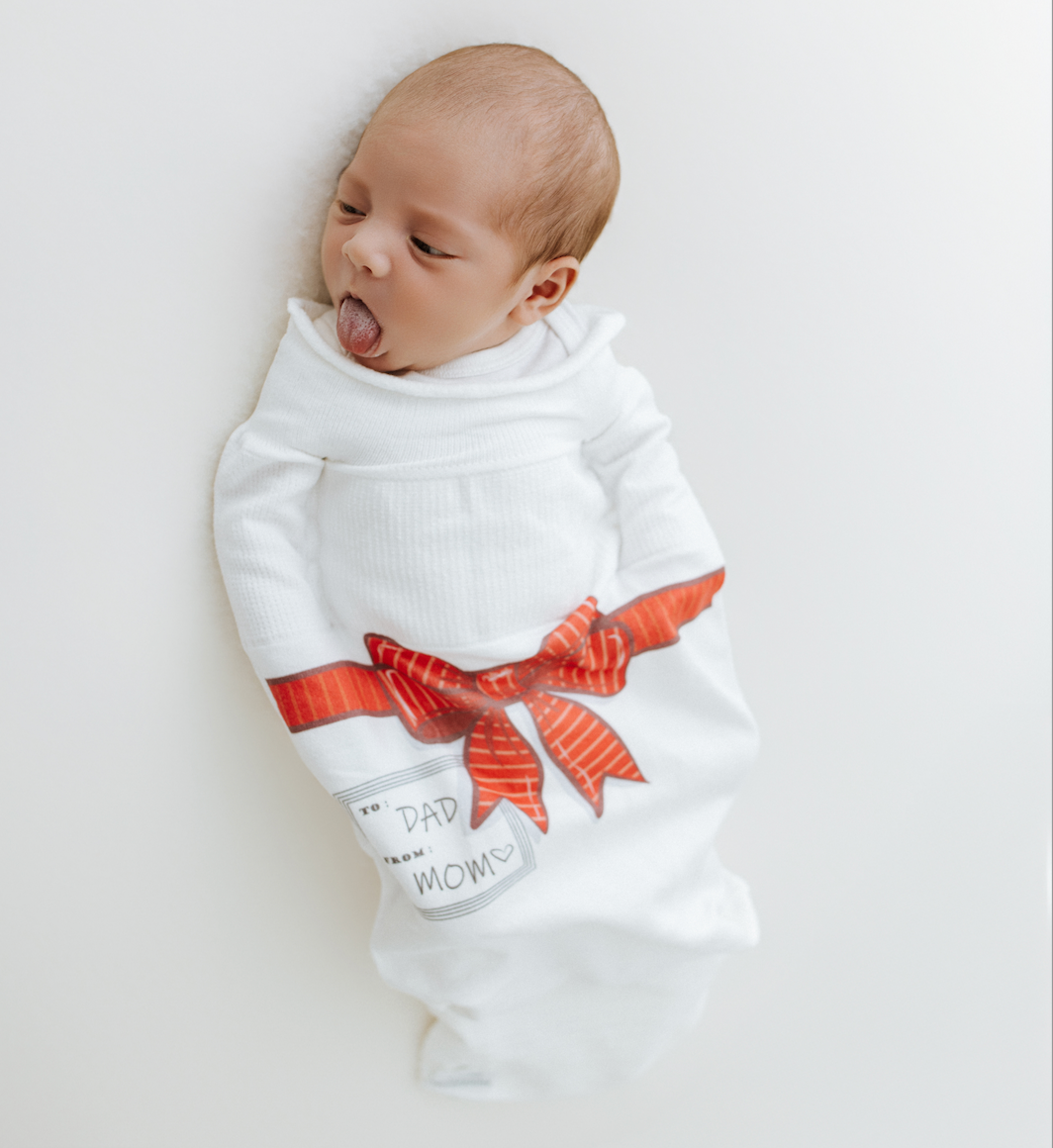 Newborn baby wrapped in a white blanket with a red bow and text on a light gray background
