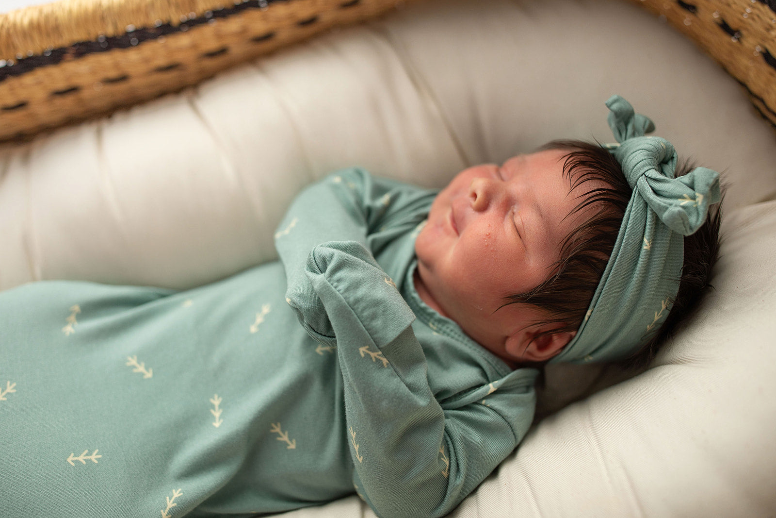 Three Little Tots Arrow Newborn Knotted Baby Gown. Ultra Soft baby gown. Little newborn girl with lots of hair in a Snuggle Me organic in a Plum and Sparrow Moses Basket. 