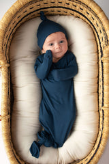 Three Little Tots Navy Blue Knotted Baby Gown. Ultra soft number 1 knotted newborn baby gown. Newborn photoshoot idea or for a pregnancy announcement. Newborn baby in a Snuggle Me Organics in a Plum + Sparrow Moses Basket 