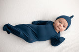 Three Little Tots Navy Blue Knotted Baby Gown. Ultra soft number 1 knotted newborn baby gown. Newborn photoshoot idea or for a pregnancy announcement. Newborn baby in a Snuggle Me Organics in a Plum + Sparrow Moses Basket 