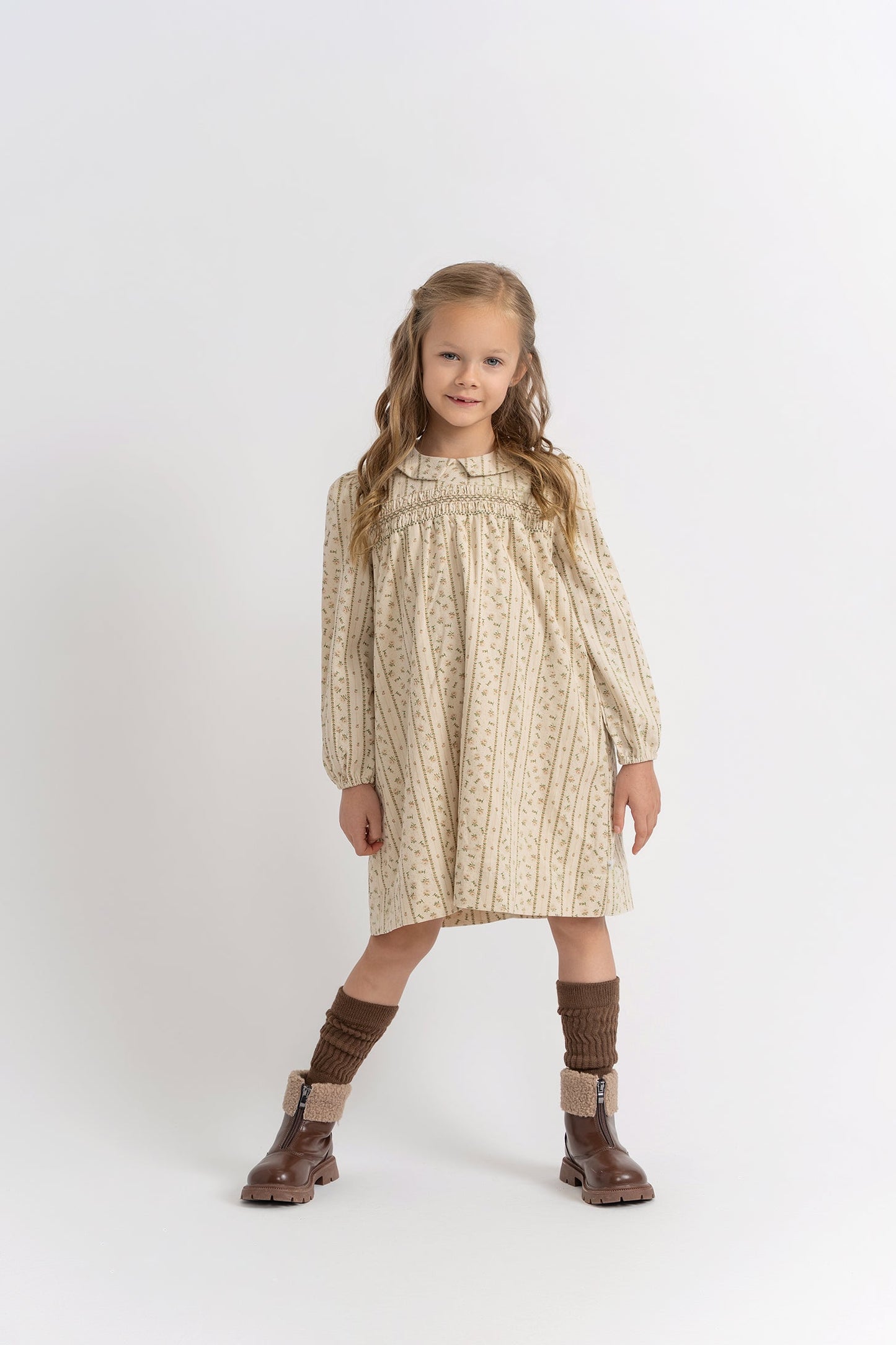 Young girl wearing a patterned dress and brown boots on a white background