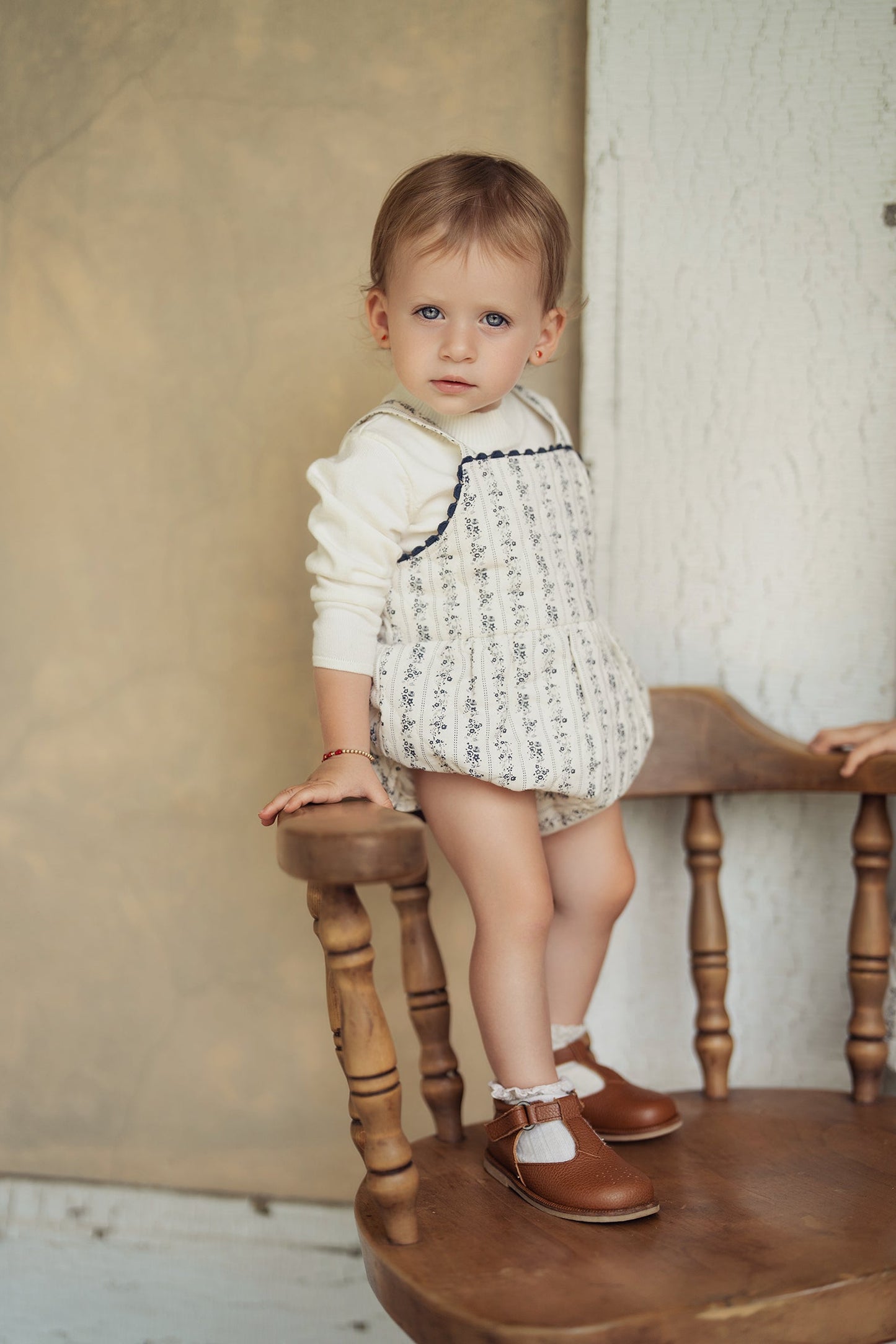 Child wearing a patterned outfit standing on a wooden stool against a neutral background
