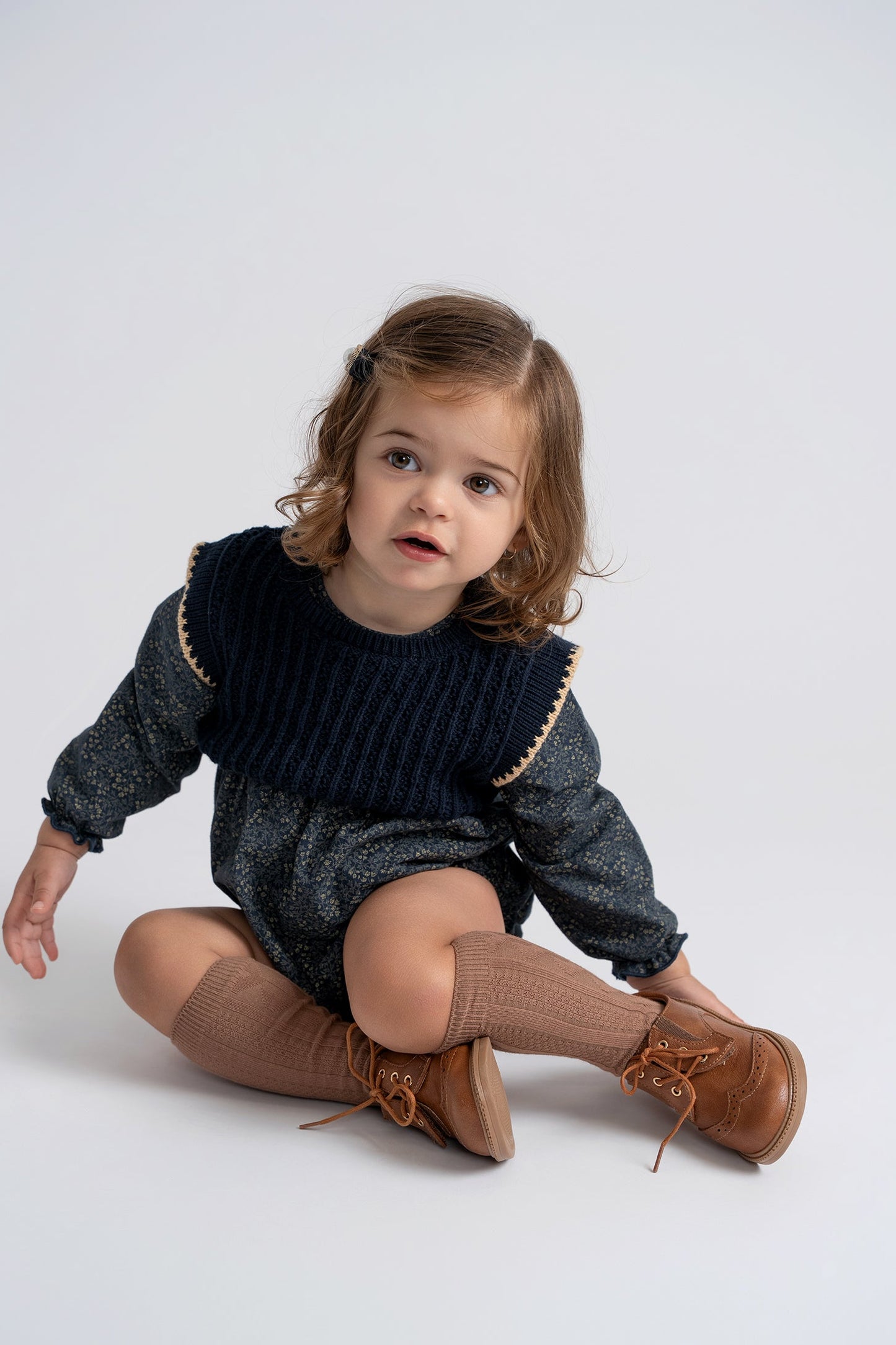 Child wearing a dark sweater with gold trim and brown shoes on a white background