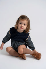 Child wearing a dark sweater with gold trim and brown shoes on a white background
