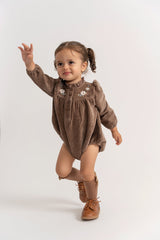 Child wearing a brown outfit with floral details on a white background