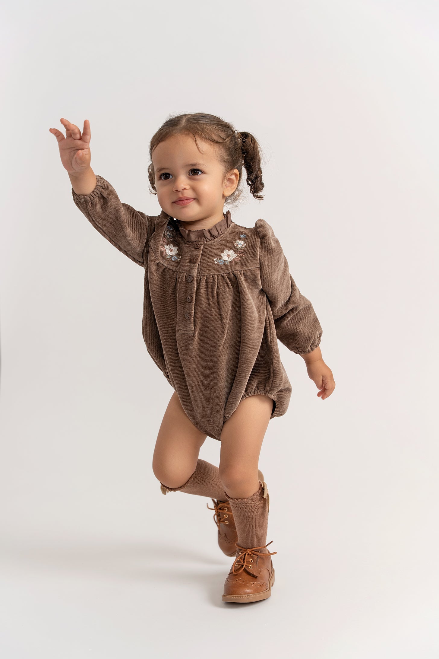 Child wearing a brown outfit with floral details on a white background