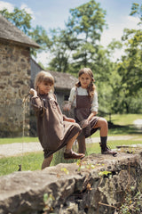 Two young girls in vintage clothing sitting on a stone wall outdoors.