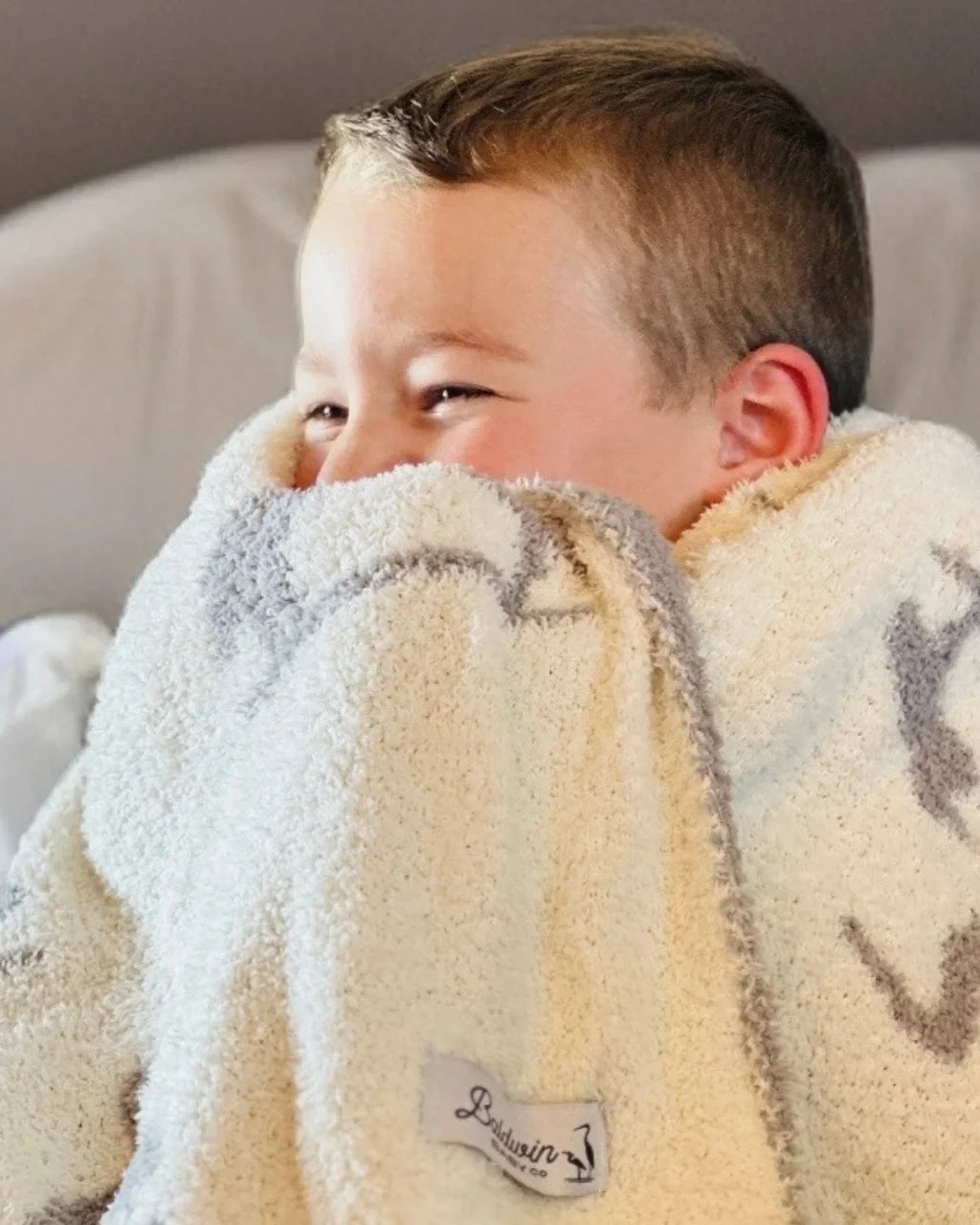 Child wrapped in a fluffy blanket with a visible brand logo on a neutral background