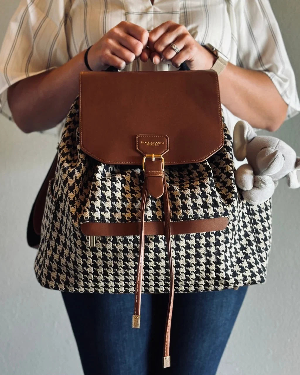 Person holding a houndstooth-patterned backpack with brown leather accents