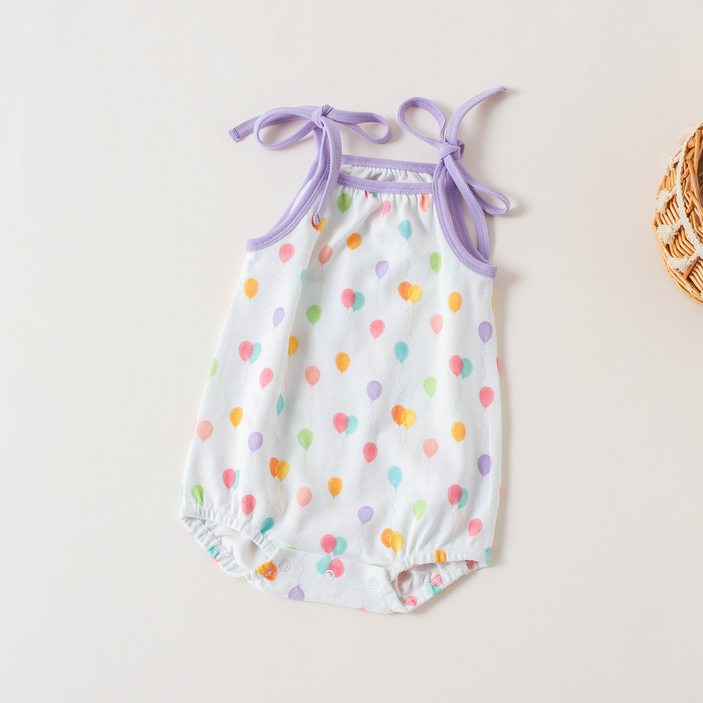 Colorful polka dot baby romper with purple straps on a light background
