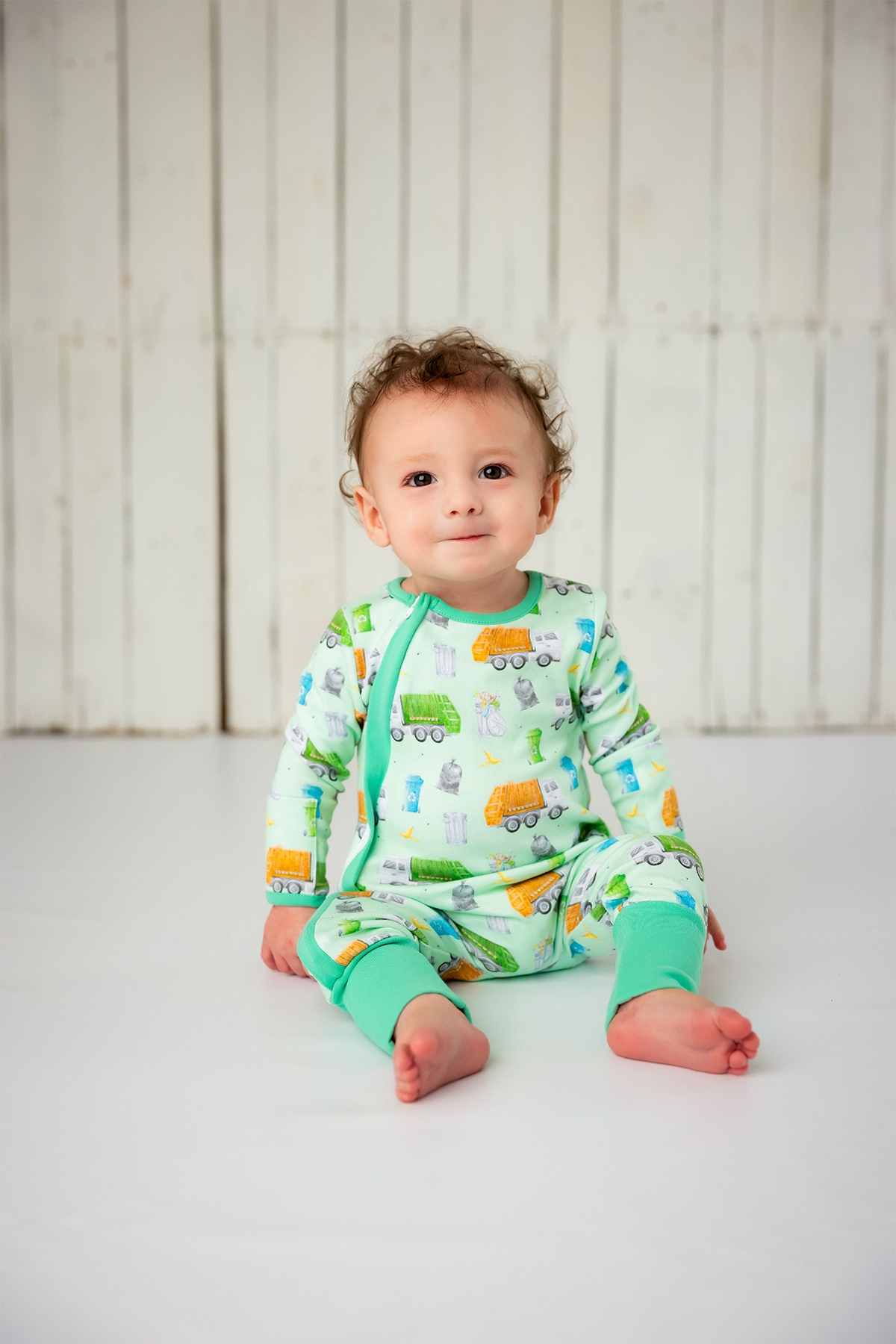 Baby wearing a colorful onesie with vehicle pattern on a white background
