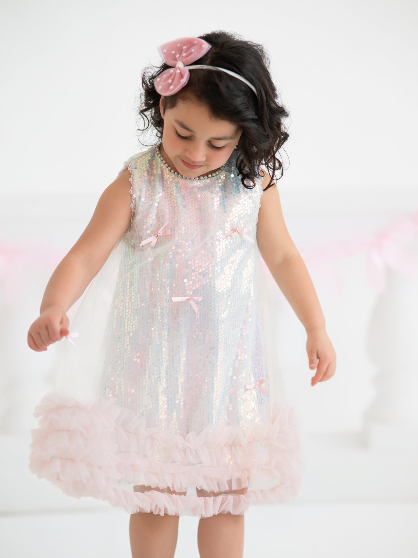 Young girl wearing a sparkling pink dress with a white background