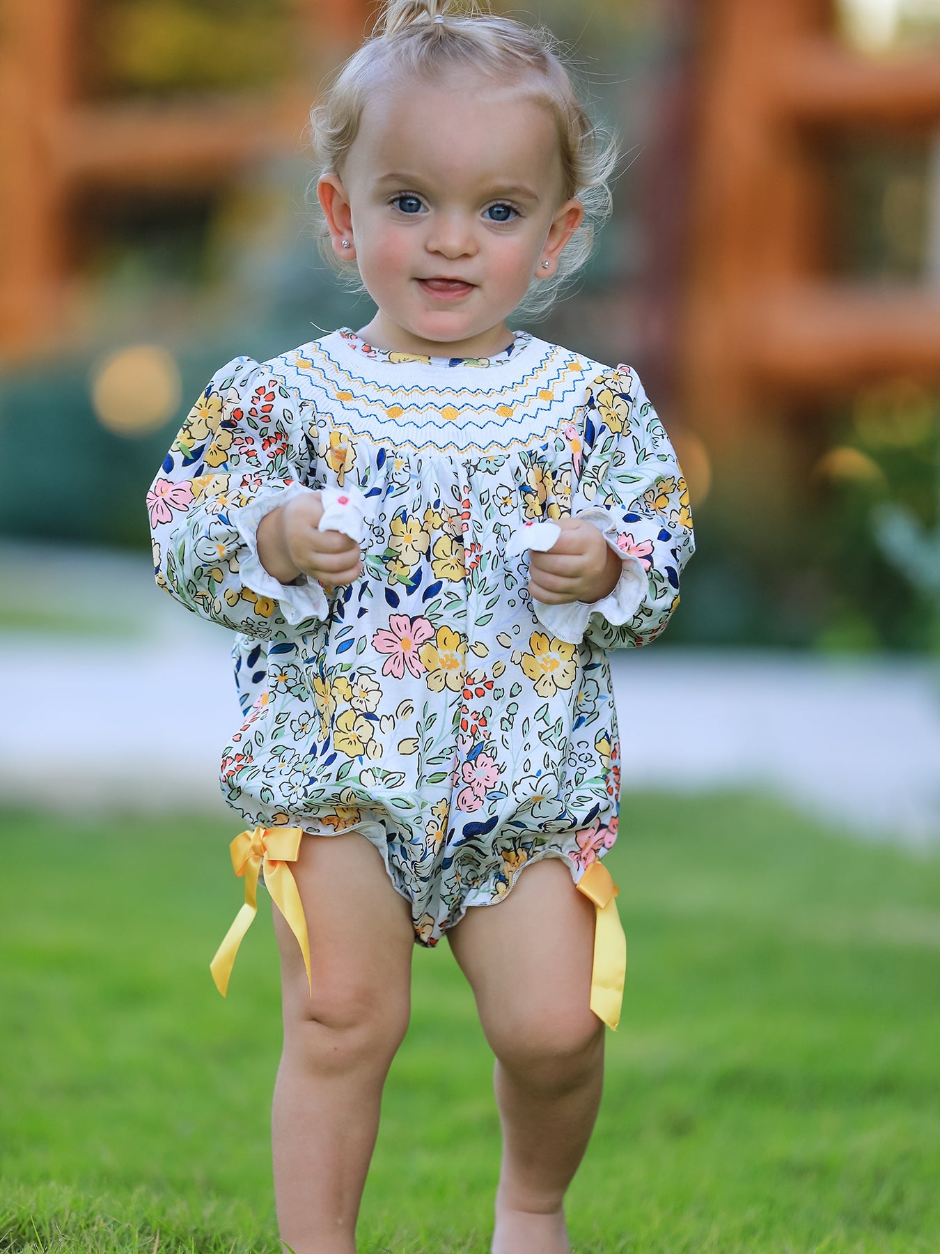 Child wearing a floral outfit with a yellow bow in an outdoor setting