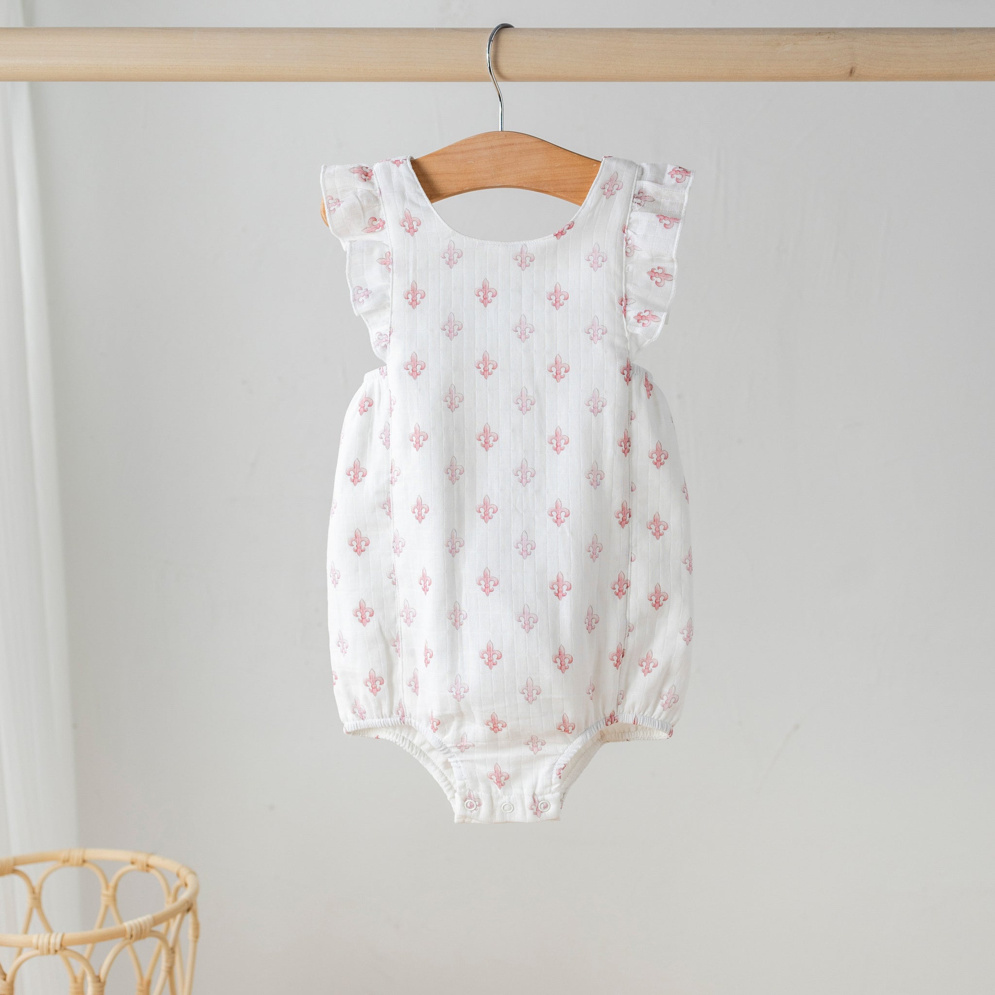 Baby romper with floral pattern hanging on a wooden hanger against a plain wall.
