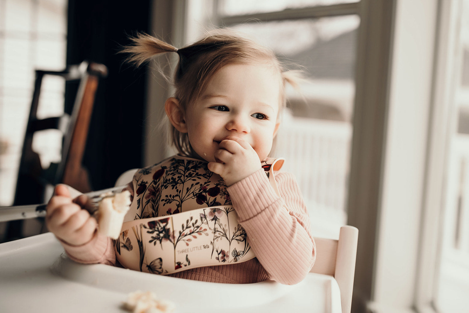 Little girl eating with a Three Little Tots floral silicone bib