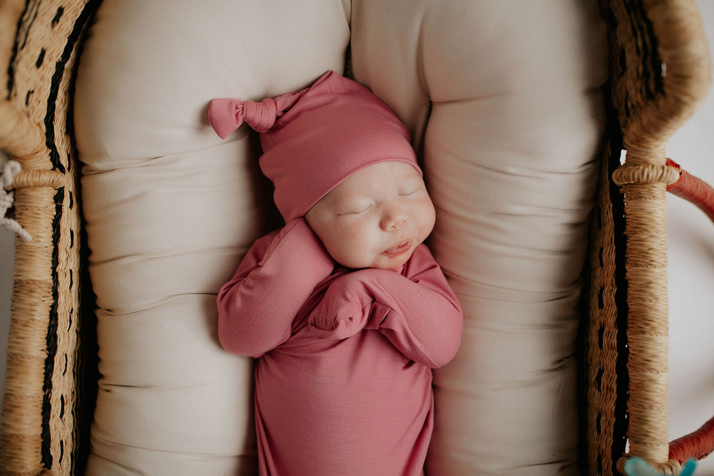 Luxuriously soft modal knotted baby gowns for newborn babies, offering comfort, easy diaper changes, and style. Three Little Tots Rose Pink Knotted baby gown. Knotted tie bottom mimics the womb to bring comfort to your newborn. Newborn baby in Snuggle Me organics in a Plum + Sparrow Moses Basket