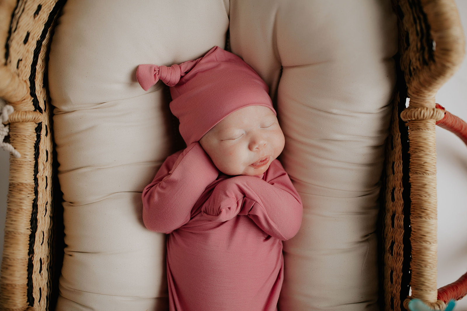 Luxuriously soft modal knotted baby gowns for newborn babies, offering comfort, easy diaper changes, and style. Three Little Tots Rose Pink Knotted baby gown. Knotted tie bottom mimics the womb to bring comfort to your newborn. Newborn baby in Snuggle Me organics in a Plum + Sparrow Moses Basket