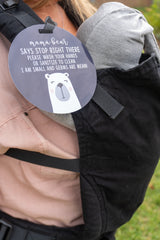 Newborn baby in a car seat carrier with a Three Little Tots no touching sign