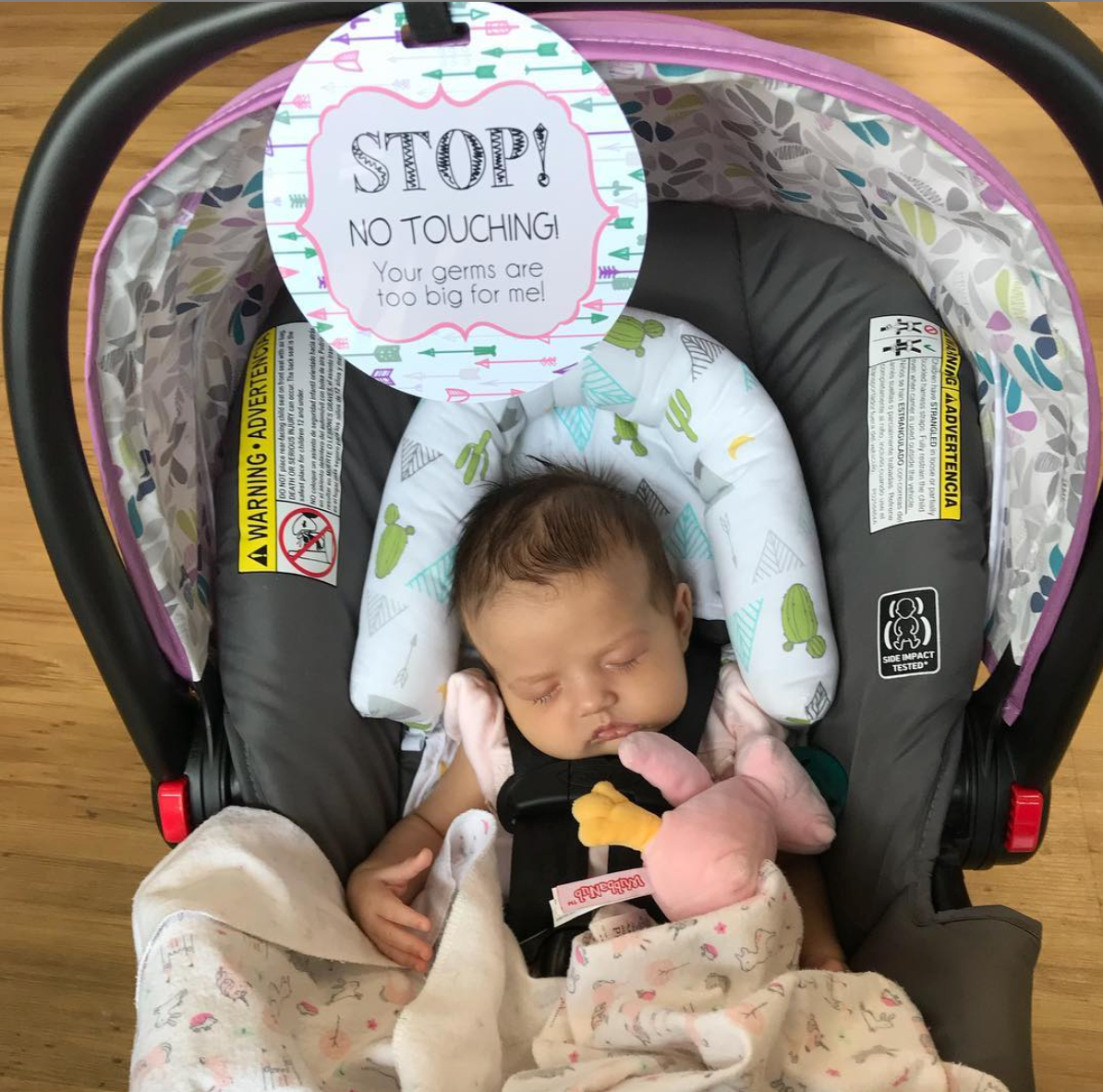 Newborn baby girl with a Three Little Tots No Touching Car seat sign