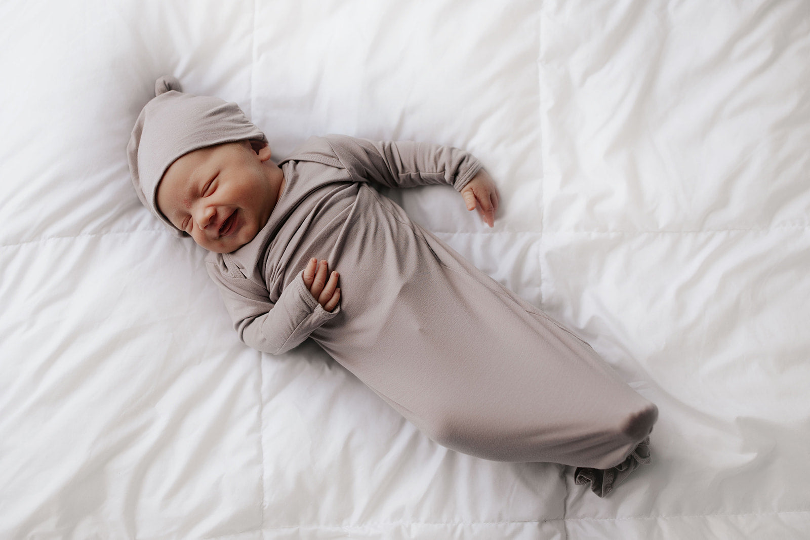 A cute newborn baby smiling in a Three Little Tots knotted gown