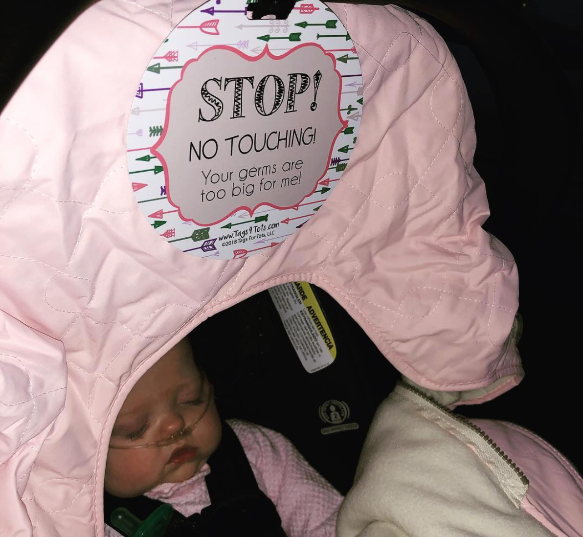 Newborn baby girl with a Three Little Tots No Touching Car seat sign