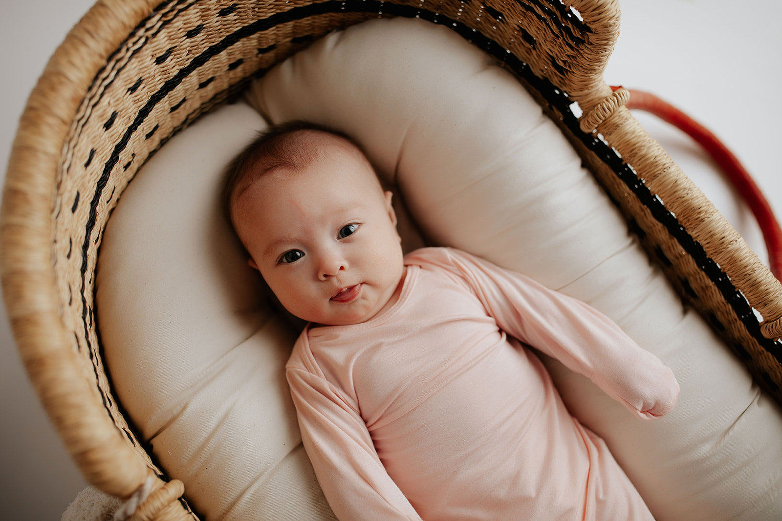 Cute newborn baby girl in heavenly pink knotted baby gown laying in a snuggle me organics. Featured the plum + Sparrow Moses Basekt