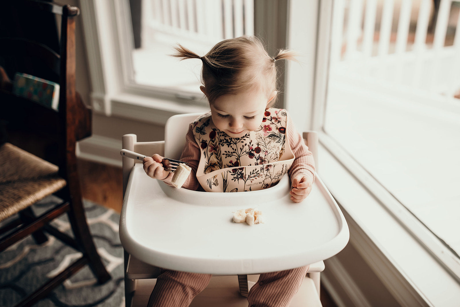 Toddler eating bananas staying clean with the Three Little Tots Floral Silicone Bib 