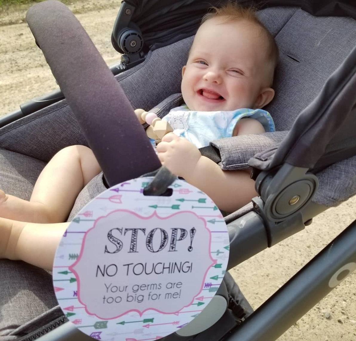 baby girl with a Three Little Tots No Touching Car seat sign on a stroller 