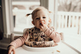 Little girl eating puffs with a Three Little Tots floral silicone bib
